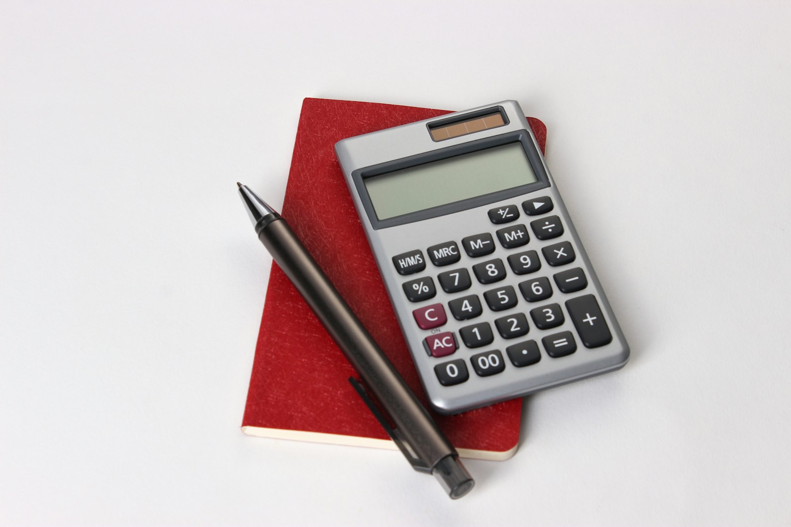 A calculator and pen resting on a red notebook