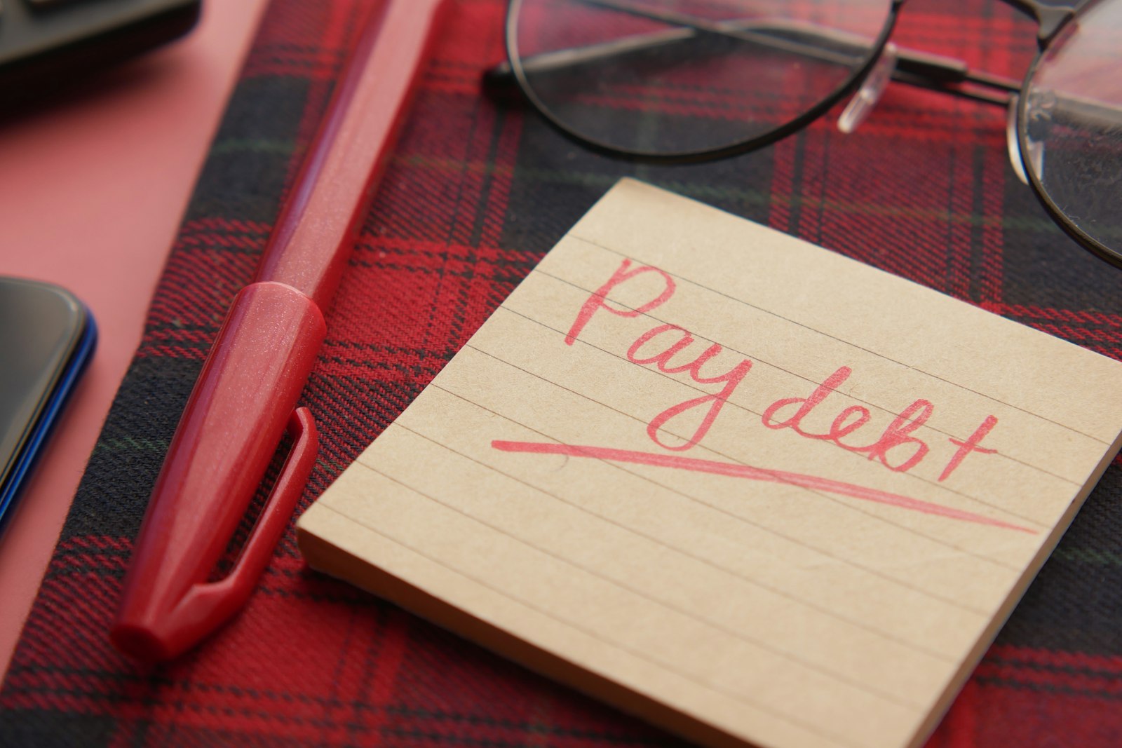 A sticky note that reads pay debt beside a pen