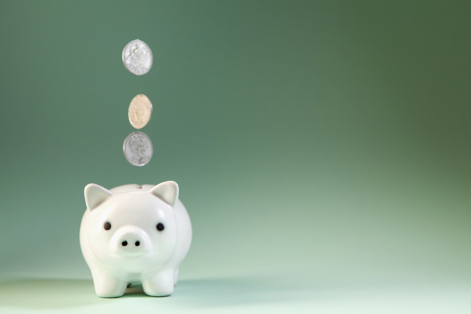 Coins dropping into a white piggy bank