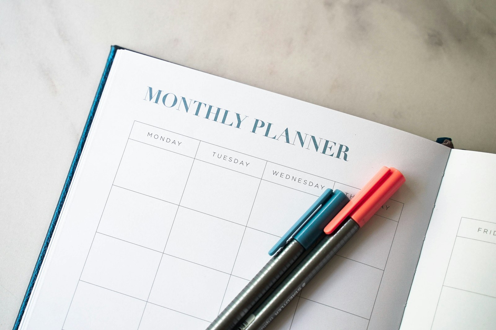 An open monthly planner with pens on a desk