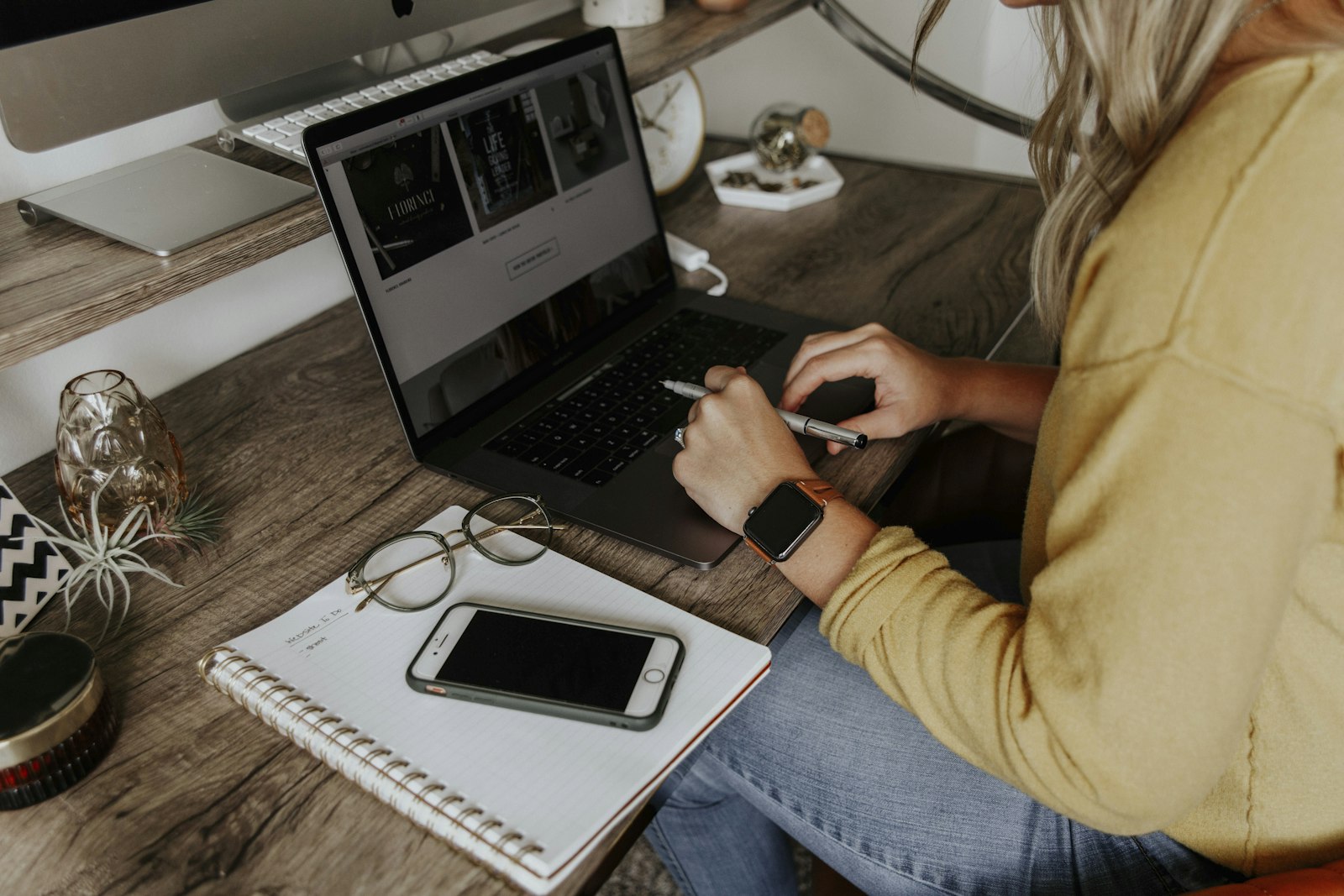 A person working on a laptop with a notebook and phone on the desk
