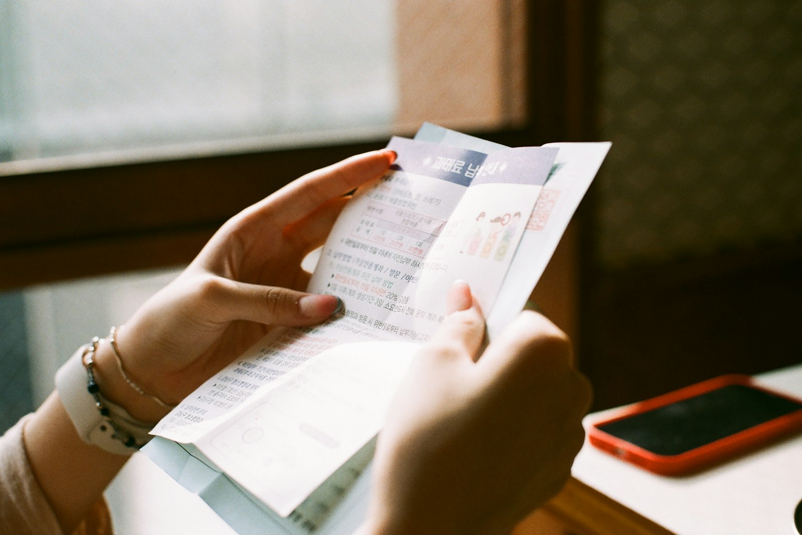 A person reading a printed bill while holding a phone